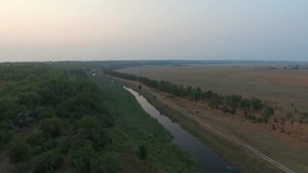 Aerial footage. River flows next to the wood. Evening.