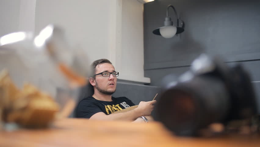 Bearded brunet sits on gray sofa in art studio.