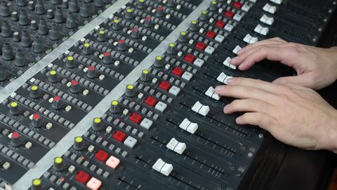 Sound mixing console, hands adjusting the faders and volume controls 