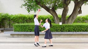 Cute Asian Thai high schoolgirls student couple in school uniform are having fun playing chasing and catching a doll with her student friend 

