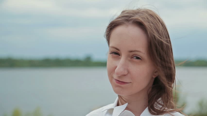 Portrait of beautiful model looking at camera in embankment, hair blowing in wind