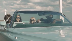 Group of young attractive teenagers having fun sitting in a retro car laughing