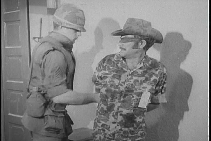 A military policeman brings a prisoner of war into a room by the scruff of  his neck, untying his wrists, leaving, locking the door behind him; inside  (1960s)