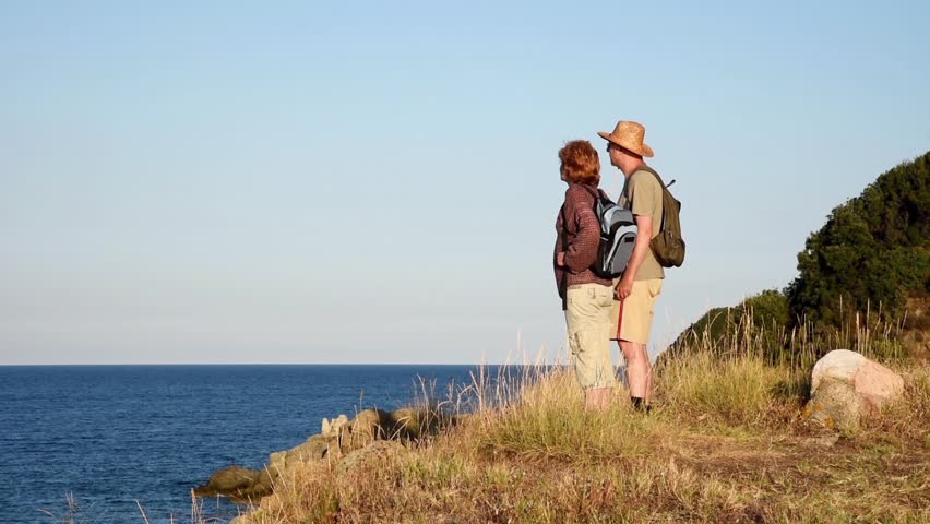 Woman and man standing on the top of the hill and enjoying the sea view in the sunset