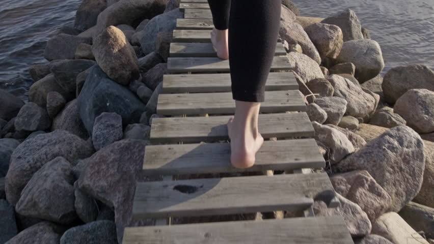 A young barefoot woman is walking out on a small jetty over the ocean in northern Sweden. Camera follows behind legs and feet. Vacation, holiday, recreation concept. Slow motion. Natural look. Royalty-Free Stock Footage #18646127