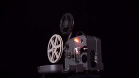 Retro movie projector on a black background. The film 8 millimeters. Moving parts and flashing light of the projector. The film is moving.