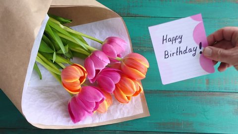 Flat lay view of Tulip flowers bouquet with Happy birthday message note on a wooden table background. Women holiday concept. copy space 