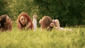 Three friends, young girls, having fun in park, laying on grass, dolly motion.