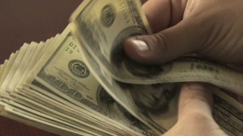 Close-up of a businessman's hands counting hundred  dollar bills at a table 