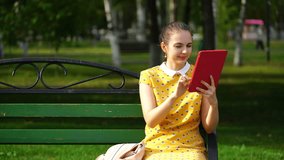 woman sitting on a bench in the park and use the application on your tablet. 4K video