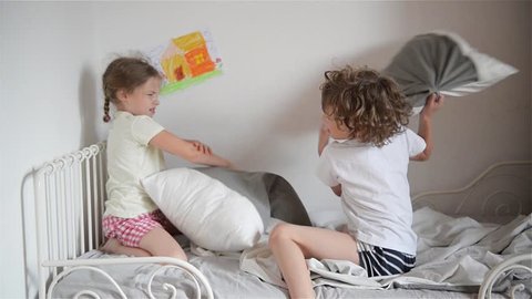 The brother and the sister have arranged fight by pillows on a bed in a bedroom.