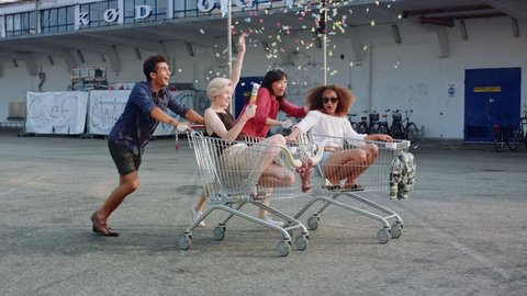 Young friends racing grocery carts. Multiracial group of young people enjoying outdoors with shopping trolley race.
