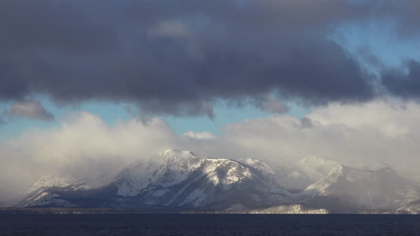 A time lapse shot of clouds moving over the snow covered mountains of Lake Tahoe in winter. (Lake Tahoe, Nevada 2010s)