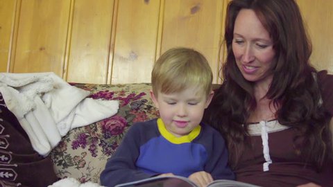 A mother sits on a couch with her boy and reads a book with her son