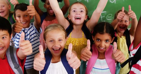 Portrait of group of diverse school kids showing thumbs up in classroom at school 4k