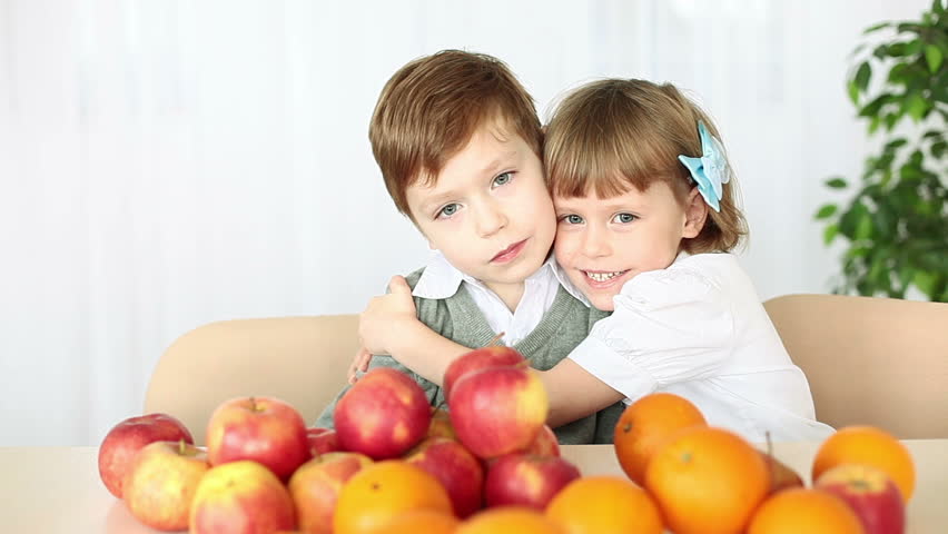 Brother and sister hugging. They sit at the table. Fruit on the table