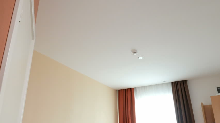 cheerful young slim blonde dressed in blue dress is jumping on snow-white bed in clear hotel room