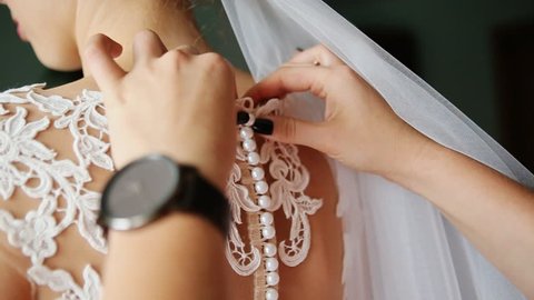 As the bride prepares for her wedding day, the maids button pearls and lace up the back of her gown 庫存影片