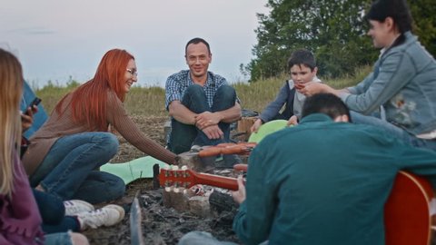 Happy friends cooking bbq near campfire and plays guitar outdoor