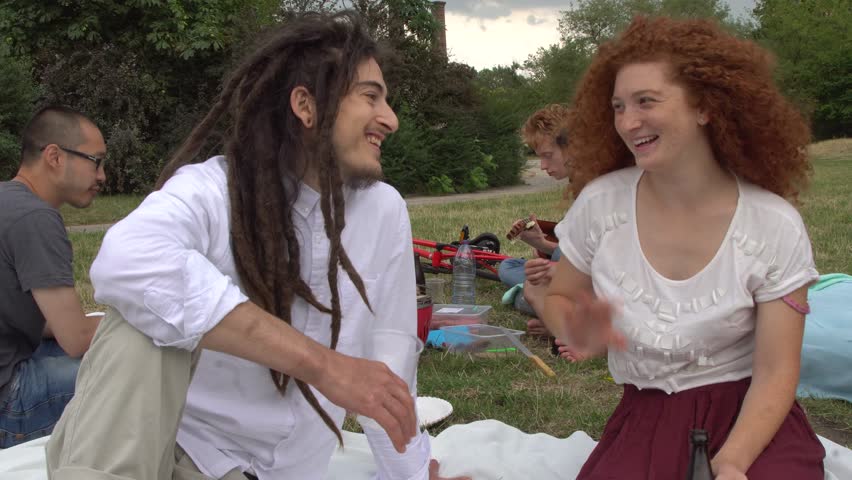 Boy with rasta dreadlocks and redhead girl flirting and chatting during picnic in park