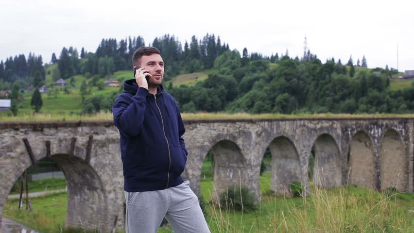 Man speaks on the phone near the old viaduct in the mountains