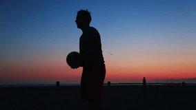 Slow motion of man's silhouette juggling soccer ball with knees at beach