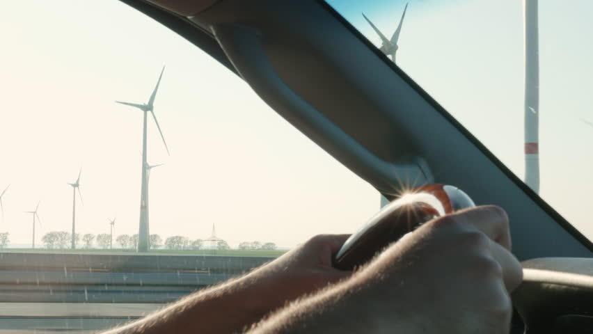 Driving in the sun and passing a wind farm, side close-up shot of hands on the wheel. | Shutterstock HD Video #18746036