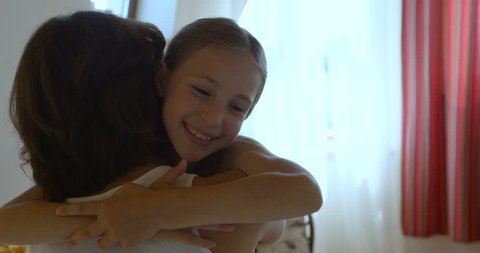 Smiling daughter rushes into mother's arms at home and gives her a big hug.