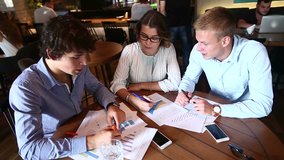 Two smart young business men one woman in suits sitting on table with documents, graphics, technology, laptop, phone, tablet. Team entrepreneurs negotiate, discuss issues, solve problems, agree, talk - Powered by Shutterstock - Get 15% off with code: PIKWIZARD15