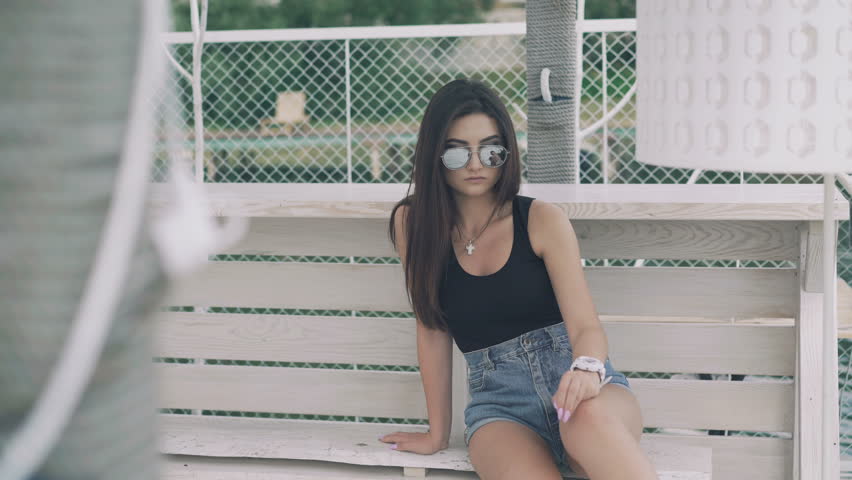 Pretty girl relaxing on a bech bench overlooking the beach in 4K