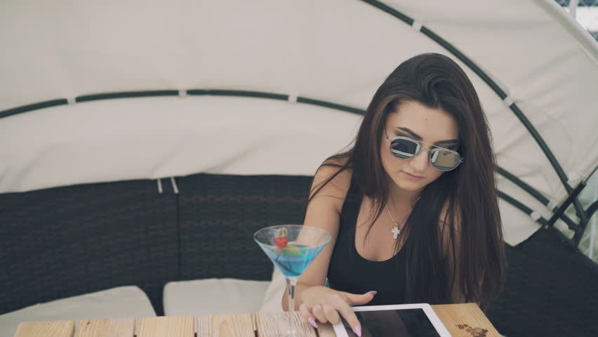 Fashionable girl uses digital tablet resting on beach lounge in 4K