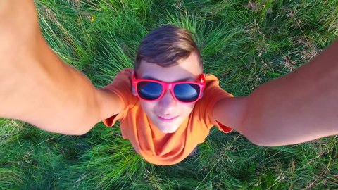 Aerial view of a boy in a red sunglasses having fun in a mountain meadow. Smiling boy is playing with drone.