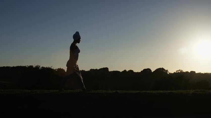 4K Silhouette of african american woman in headscarf walking and enjoying the sunset