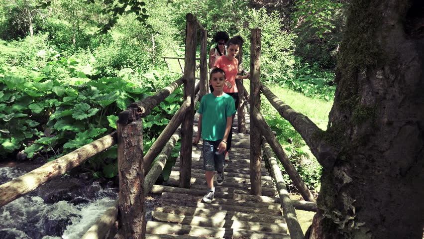 Hikers walking old bridge in rain forest jungle. Hiking family trekking through dense reinforced nature. Healthy young sporty multiracial family living active lifestyle