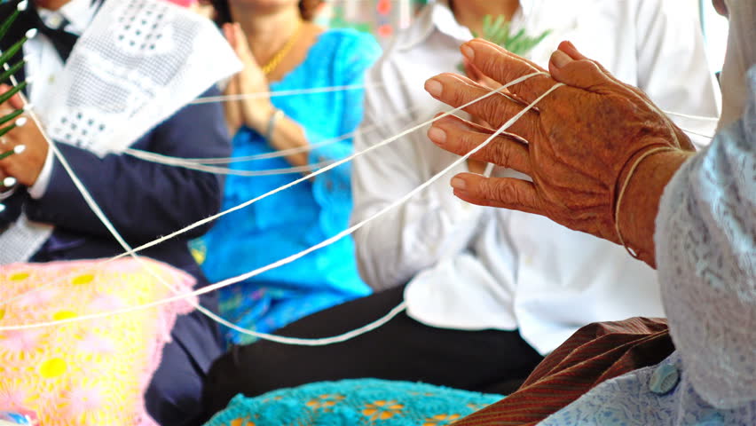 Focus on old woman hand praying and holding white thread of Thai blessing ceremony for marriage celebration