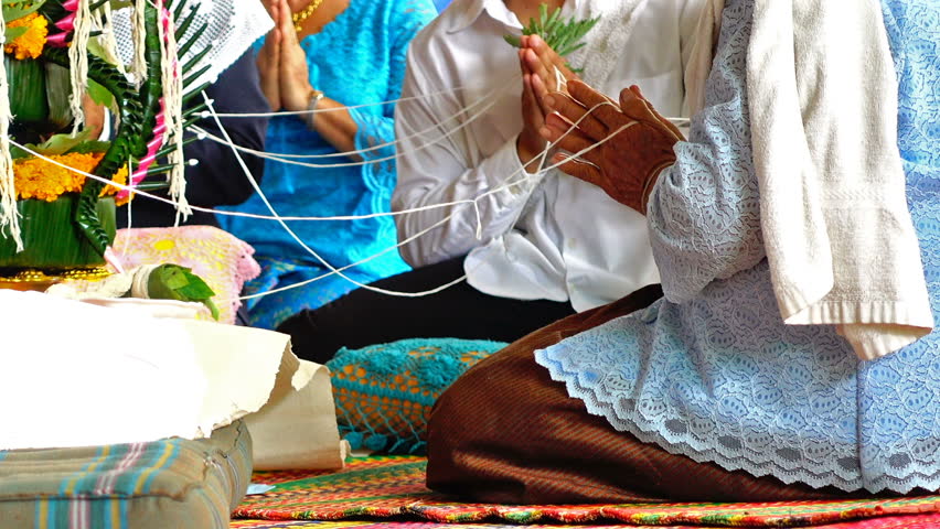 Focus on old woman hand praying and holding white thread of Thai blessing ceremony for marriage celebration