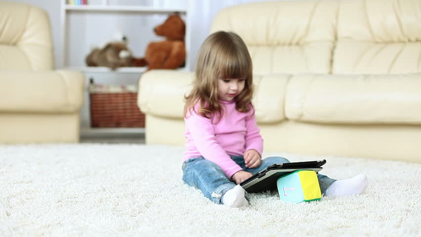 Baby girl holding a tablet and sits on the floor