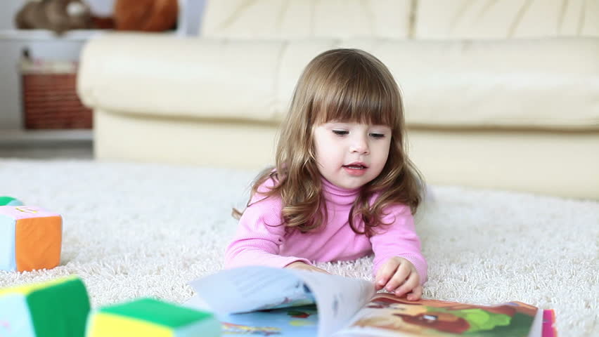 Baby girl reading a book while lying on the floor
