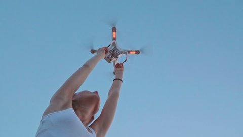 SLOW MOTION 240 fps: Drone is taking off from woman's hands. Young woman releasing copter to fly in the sunset field. Modern technology in our life.