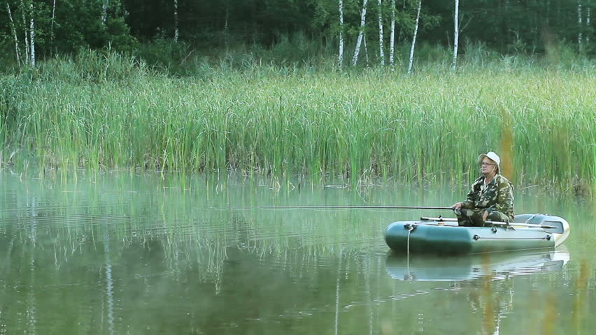 The fisherman floats on a lake on an inflatable boat with a fishing rod. Early morning with fog on the water. vacation in the wild