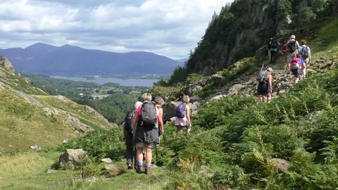 Big group of senior people with backpacks and walking poles hiking in picturesque Cumbria, Lake District, England.Slow motion