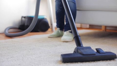 people, housework and housekeeping concept - woman with vacuum cleaner cleaning carpet at home