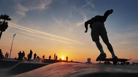 Silhouette of skater on skateboard jumping over sunset sky at Venice Beach skate park, California. Slow motion.