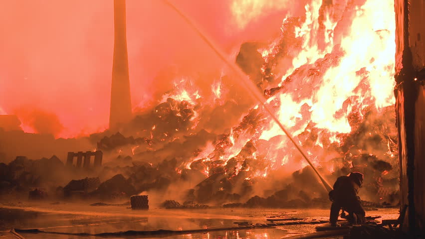 Wide shot of an industrial fire being fought by firemen