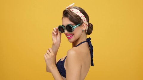 Sexy young gorgeous pinup girl showing silence gesture, taking off her sunglasses and winking