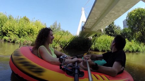 Happy couple sail in inflatable boat sail under bridge and makes selfie
