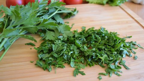 Parsley and vegetables ingridients on the cutting wooden kitchen board on the table. Cooking workspace on the kitchen.