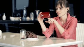 Happy woman watching movie on smartphone sitting by table in kitchen
