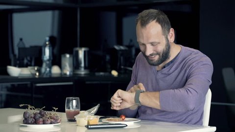 Young man using smartwatch during breakfast in kitchen at home

