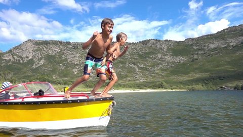 children jump and dive into the water from a boat in slow motion